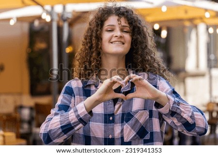 I love you. Young woman makes symbol of love, showing heart sign to camera, express romantic feelings, express sincere positive feelings. Charity, gratitude, donation. Outdoors in urban city street