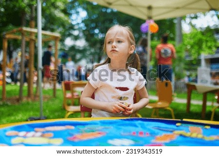 Adorable preschooler girl playing board game outdoors. Unhappy child not liking to lose Royalty-Free Stock Photo #2319343519