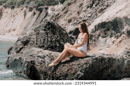 Woman travel sea. Happy tourist in white bikini enjoy taking picture outdoors for memories. Woman traveler posing on the beach at sea surrounded by volcanic mountains, sharing travel adventure journey