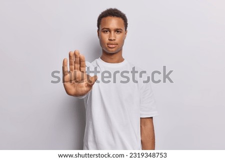 Waist up shot of serious dark skinned man raises his hand in firm stop gesture reminding us of importance of setting boundaries and taking pause dressed casually isolated over white background. Royalty-Free Stock Photo #2319348753