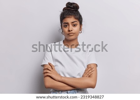 Studio shot of serious Indian woman with dark hair combed in bun keeps arms folded waits for explanations listens attentively information dressed in basic t shirt isolated over white background. Royalty-Free Stock Photo #2319348827