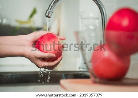 An Asian woman washes apples in the kitchen.