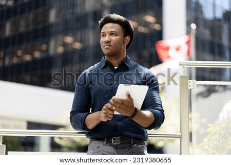Portrait of serious African American man holding digital tablet, planning project, looking away standing on urban street. Successful business   Royalty-Free Stock Photo #2319380655