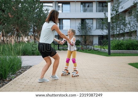 Mother helps daughter learn to roller skate. 