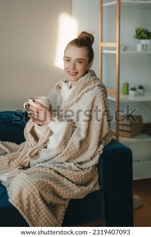 Attractive woman with natural ginger hair looking at camera with white cup of hot drink, wrapped with blanket at home. Drinking tea or coffee, dreaming Royalty-Free Stock Photo #2319407093