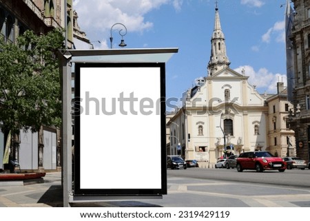 bus shelter blank ad panel. billboard display. empty white lightbox sign at bus stop. glass structure. transit station. mockup base. urban city street setting with car traffic. bus shelter advertising