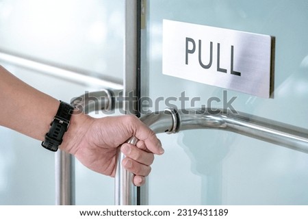 Close up male hand holding stainless steel handle opening glass door in office building. Silver metal aluminum pull sign