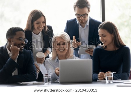 Happy senior mentor, coach teaching excited diverse interns, students showing and explaining online virtual video presentation on laptop, watching and discussing funny webinar, teaching new employees Royalty-Free Stock Photo #2319450313
