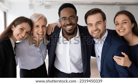 Happy multiethnic different aged business group celebrating corporate success, high teamwork result, team achieve, feeling joy, hugging together, looking at camera, smiling. Headshot portrait
