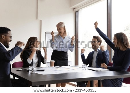 Happy excited diverse millennial team with mature business leader celebrating business success, win, achieve. Team of interns and senior mentor making winner gestures, laughing, shouting for joy Royalty-Free Stock Photo #2319450355