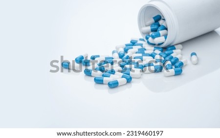 Blue-white antibiotic capsule pills spread out of plastic drug bottles. Antibiotic drug resistance. Prescription drugs. Healthcare and medicine. Pharmaceutical industry. Pharmacy product. Medication. Royalty-Free Stock Photo #2319460197