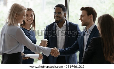 Happy confident senior businesswoman, business leader, coach getting acquainted with new team of employees, interns, students, standing and shaking hands with worker at informal meeting Royalty-Free Stock Photo #2319461013