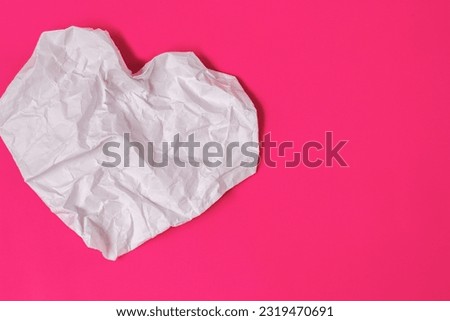 heart-shaped crumpled white paper on a pink background