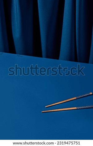 Wooden chopsticks set against a deep blue background with a blue curtain. Perfect for an Asian restaurant menu or a modern still life composition. Royalty-Free Stock Photo #2319475751