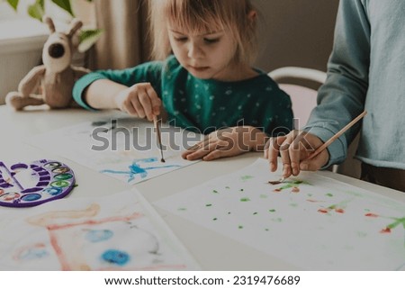 Two cute little sisters, classmates are painting on table. Small preschool and school girl. Kids use brush in kindergarten or school. Adorable preschooler in living room. Home schooling concep