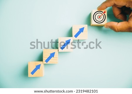 Wooden blocks featuring a Target icon atop rise up arrows. Bar graph chart steps showcase business growth on a blue background, highlighting profit, investment, and economic improvement concepts.