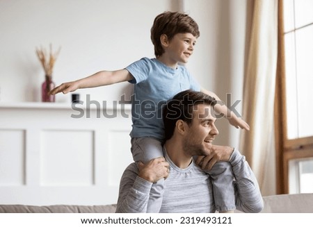 Overjoyed Caucasian dad carry on back engaged in funny game activity with little 6s son on family weekend at home. Happy caring young father relax rest have fun play with overjoyed cute boy child. Royalty-Free Stock Photo #2319493121