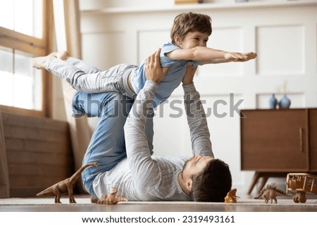 Loving young Caucasian father lying on floor at home have fun play with cute excited little son. Caring dad imitate plane fly, engaged in funny game together with happy small preschooler boy child. Royalty-Free Stock Photo #2319493161