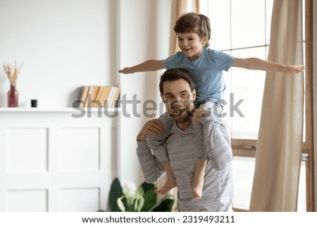 Caring young Caucasian father hold on back excited small 6s son have fun feel playful on family weekend at home. Happy loving dad play involved in funny game activity with little boy child together. Royalty-Free Stock Photo #2319493211
