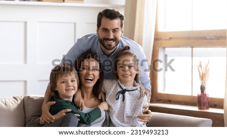 Portrait of happy young Caucasian family with two teen children sit relax on sofa in living room enjoy weekend together. Smiling parents rest on couch at home with small kids have fun indoors. Royalty-Free Stock Photo #2319493213