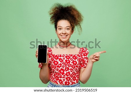 Young smiling woman she wearing casual clothes red blouse hold in hand use mobile cell phone with blank screen workspace area point aside isolated on plain pastel light green color background studio