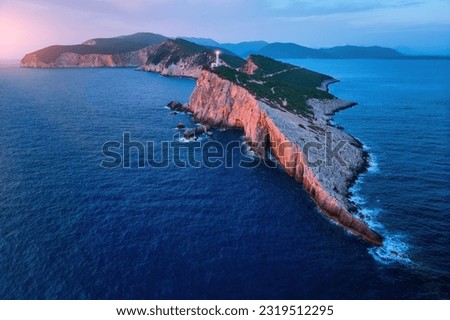 Aerial, panoramic view of White lighthouse on Cape Ducato, Lefkada Island, Greece. Shining White lighthouse on the cliff, colorful scenery, cape cliffs red illuminated by setting sun.
