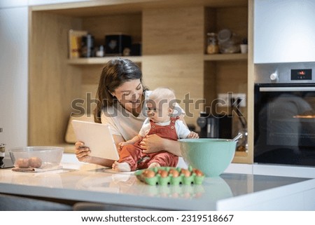 Mom plays her baby a cartoon as she holds her on the kitchen counter