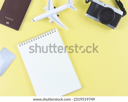 Top view or flat lay of blank page opened notebook, airplane model, passport, credit card and digital camera on yellow  background with copy space.