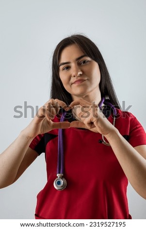 Young pretty female doctor in red uniform showing heart symbol shape with hands on white background, healthcare concept