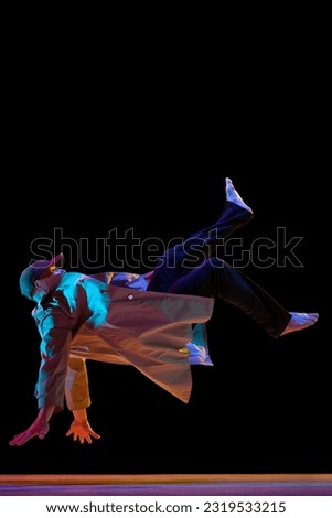 Dynamic image of young talented man in stylish clothes dancing breakdance, hip-hop over black studio background in neon light. Concept of art, street style dance, fashion, youth, hobby, dynamics, ad