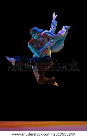 Dynamic image of young talented man in stylish clothes dancing breakdance, hip-hop over black studio background in neon light. Concept of art, street style dance, fashion, youth, hobby, dynamics, ad
