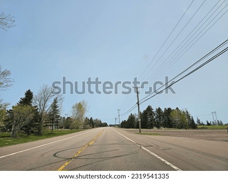 An open highway through a rural area on a clear spring day with tire marks in the road.