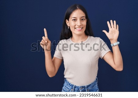 Young hispanic woman standing over blue background showing and pointing up with fingers number six while smiling confident and happy. 