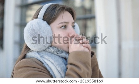 Young blonde woman blowing on hands for cold at street Royalty-Free Stock Photo #2319558169