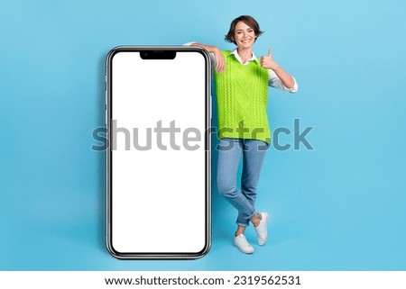 Full length photo of pretty woman with bob hairstyle green waistcoat stand near smart phone thumb up isolated on blue color background