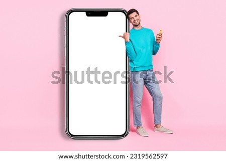 Full body photo of handsome young guy beaming smile hold gadget finger point banner wear trendy blue look isolated on pink color background