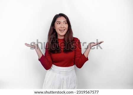 Excited Asian woman wearing red t-shirt, pointing at the copy space beside her, isolated by white background Royalty-Free Stock Photo #2319567577