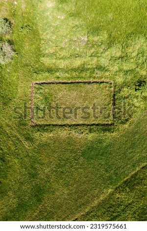 Aerial shot of unfinished house foundation in grass field from drone pov, rectangular shape in meadow as social media background image, top view