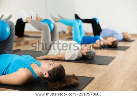 People of different ages pressing core and clutching mini Pilates balls between legs during Pilates training together
