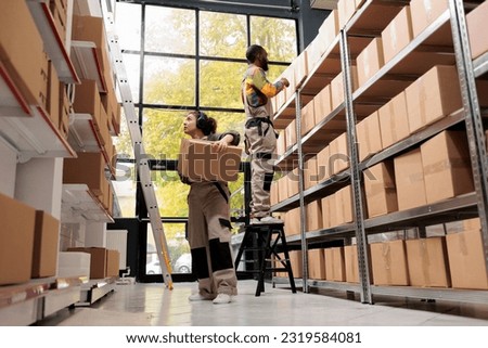 Manager carrying cardboard boxes preparing clients orders, working at merchandise inventory in warehouse. Diverse storage room team checking customers details for goods delivery. Storehouse concept