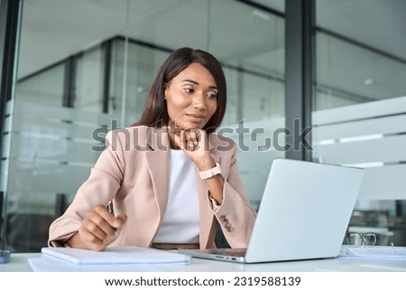 Busy professional young African American business woman company manager executive wearing suit working in office looking at laptop computer watching webinar writing notes sitting at desk. Royalty-Free Stock Photo #2319588139