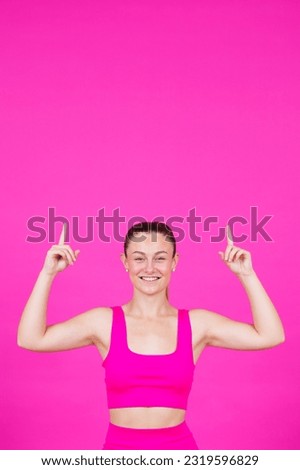 Smiling pretty sportswoman pointing up to pink copy space. Young woman looking at camera and showing message