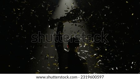 Silhouette of race car driver celebrating the win in a race against bright stadium lights, rising a trophy over his head Royalty-Free Stock Photo #2319600597
