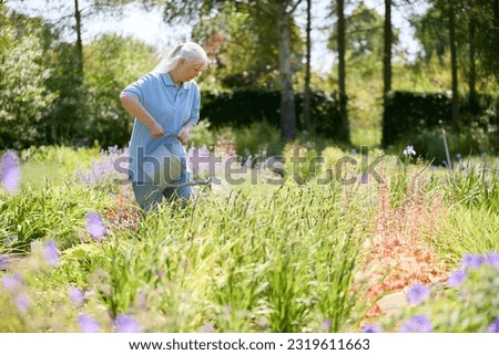 Retired Senior Woman Working Part Time Job In Garden Centre Watering Plants Royalty-Free Stock Photo #2319611663