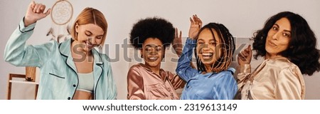 Positive multiethnic girlfriends in colorful pajama dancing and having fun while spending time together during pajama party at home, bonding time in comfortable sleepwear, slumber party, banner Royalty-Free Stock Photo #2319613149