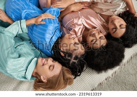 Top view of multiethnic girlfriends in colorful pajama laughing and hugging while lying on bed during pajama party in bedroom at home, bonding time in comfortable sleepwear, slumber party Royalty-Free Stock Photo #2319613319
