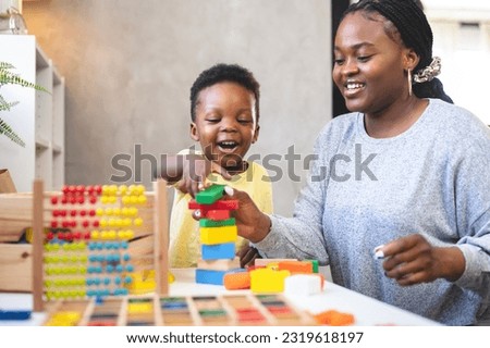 A cute little African child plays with colorful didactic educational toys. His proud mother supports him. Kindergarten teacher with child. Royalty-Free Stock Photo #2319618197