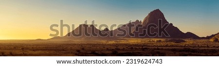 Wide panorama of a stone desert at sunrise in haze  of soft sunlight, mountain landscape of Spitzkoppe hills, Namibia. Travel to wildlife of Africa, extreme tour, adventures to wilderness.  Royalty-Free Stock Photo #2319624743