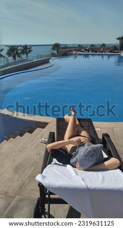 Woman is sunbathing on the edge of the pool. Blue sky and water. Relax.