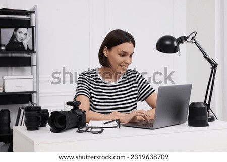 Young professional photographer with camera working on laptop in modern photo studio